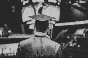 Online Students Make Great Alumni - Picture of graduate in cap and gown standing in an arena, black and white photo