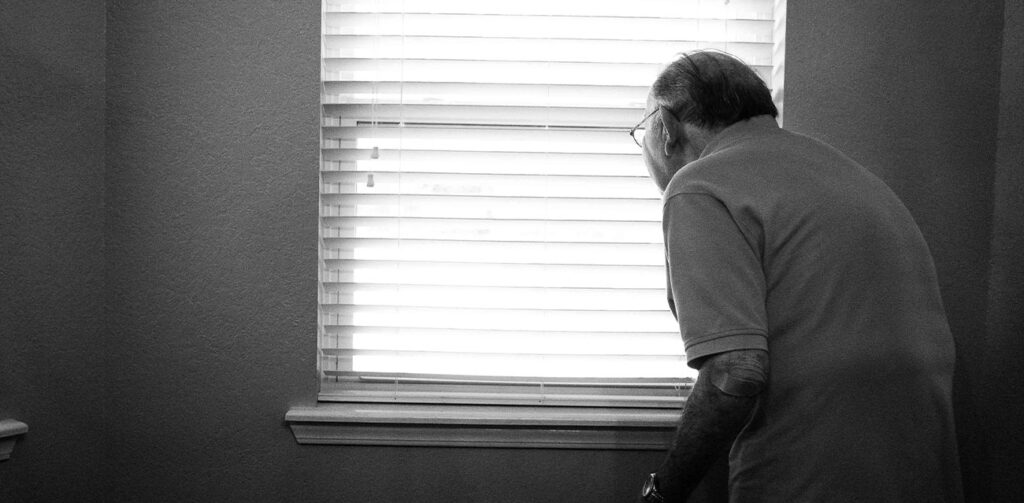 Perennial Seniors on Campus - Picture of an elderly man looking out of a window, photo in black and white